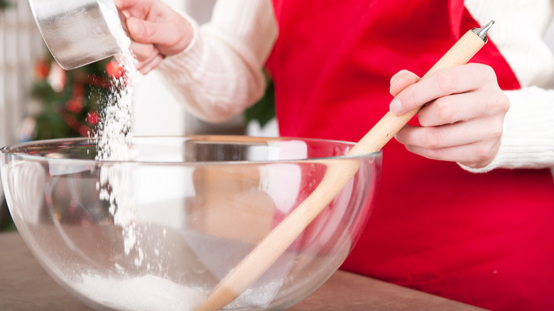 A woman pouring dry ingredients into a glass mixing bowl