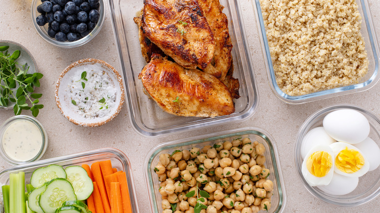 Muliple glass containers with food inside, including chicken, eggs, and chickpeas