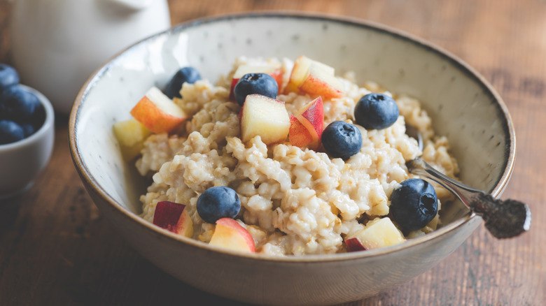 A bowl of oatmeal sits on a wooden counter, topped with slices of apple and fresh blueberries.