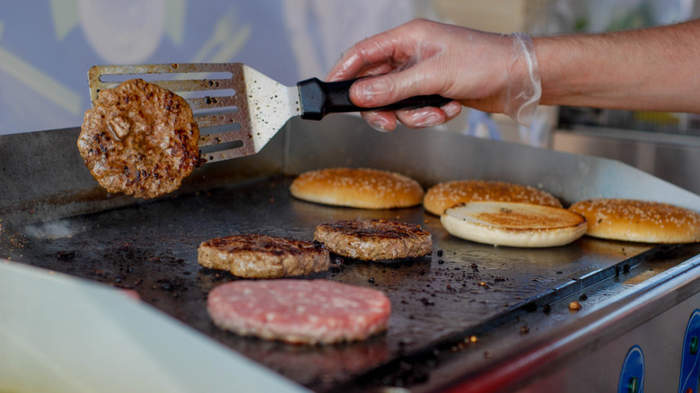 A restaurant worker flips a burger on the grill