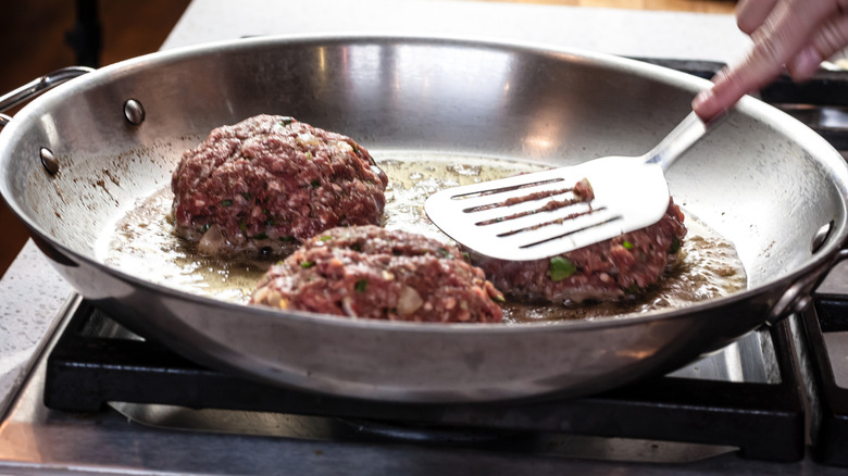 Flattening burgers in a frying pan with a metal spatula