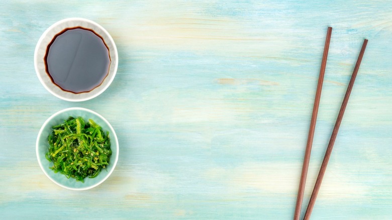 White bowls of tamari and fresh seaweed next to chopsticks