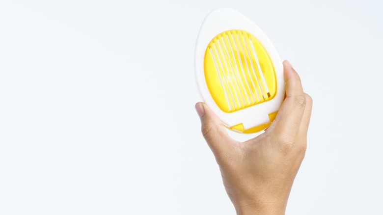 Egg slicer held up by a hand against white background