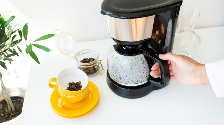 A person making coffee in a drip coffee maker with two yellow cups nearby