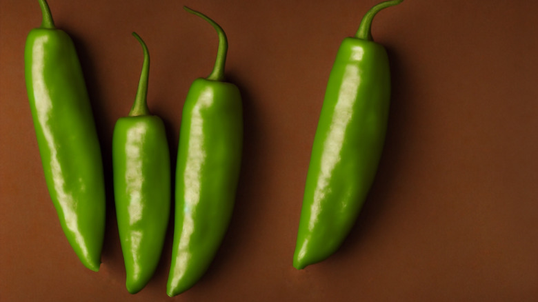 Whole green jalapeños on a brown surface