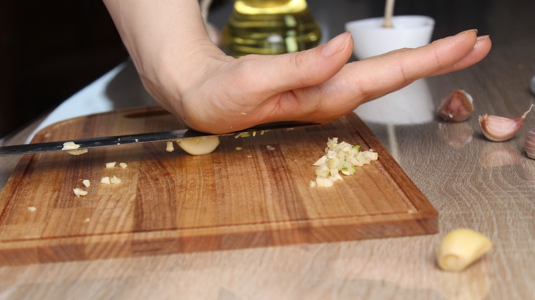 A cook crushing garlic cloves with a knife