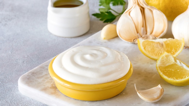 Garlic sauce, fresh garlic, and lemon wedges on a cutting board