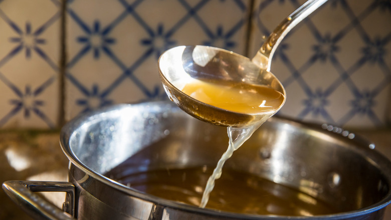 Ladling broth into a silver pan on stove