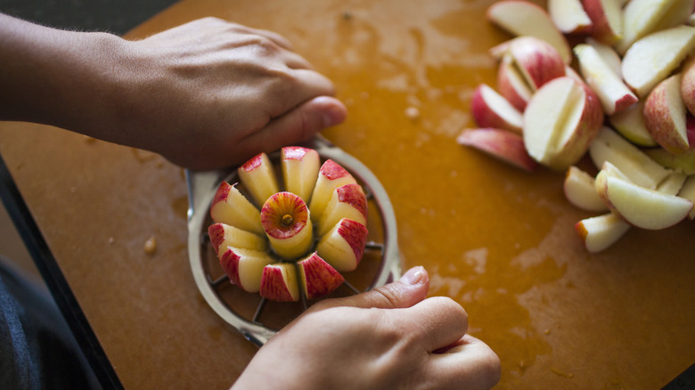 Person using an apple slicer next to a pile of sliced apples