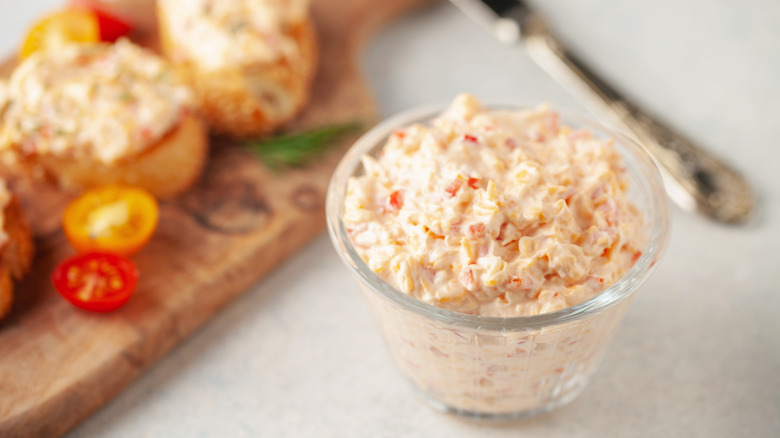 A dish of pimento cheese sitting next to a cutting board with food