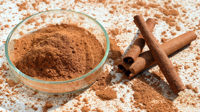 Clear bowl of ground cinnamon with cinnamon sticks