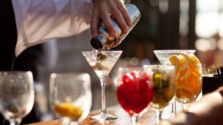 A bartender pouring a glass of martini from a shaker.