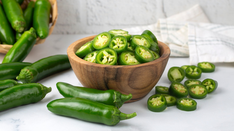 Wooden bowl of sliced fresh jalapeños alongside whole peppers