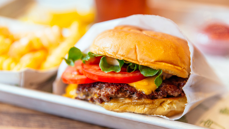 a cheeseburger sticks out of a paper wrapper on a tray next to a basket of french fries