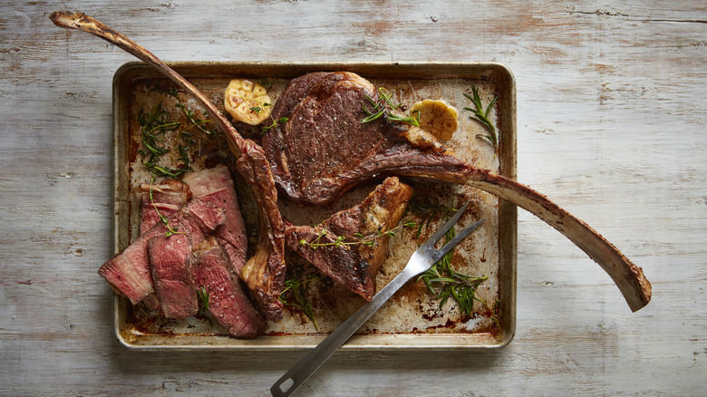 Whole and sliced tomahawk steaks on a tray alongside some garlic