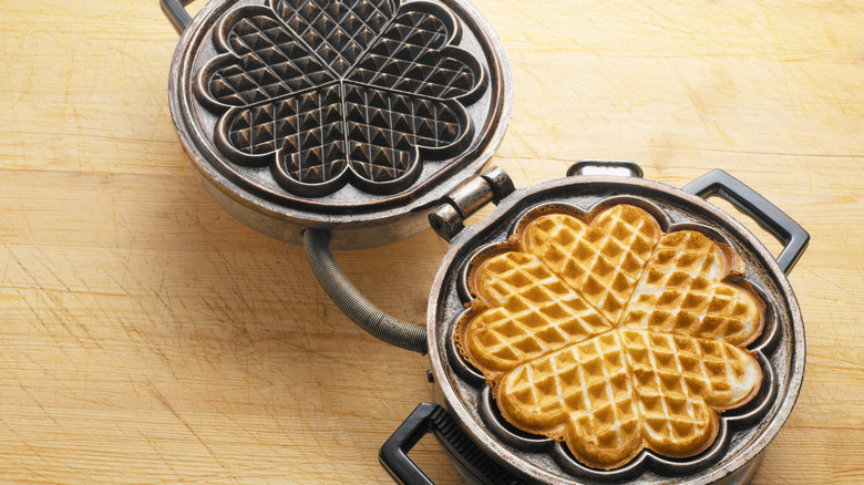 A large cooked waffle within a waffle maker with a flower design