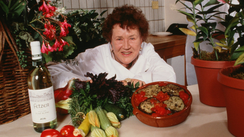 Julia Child in a chef coat sitting by a table.