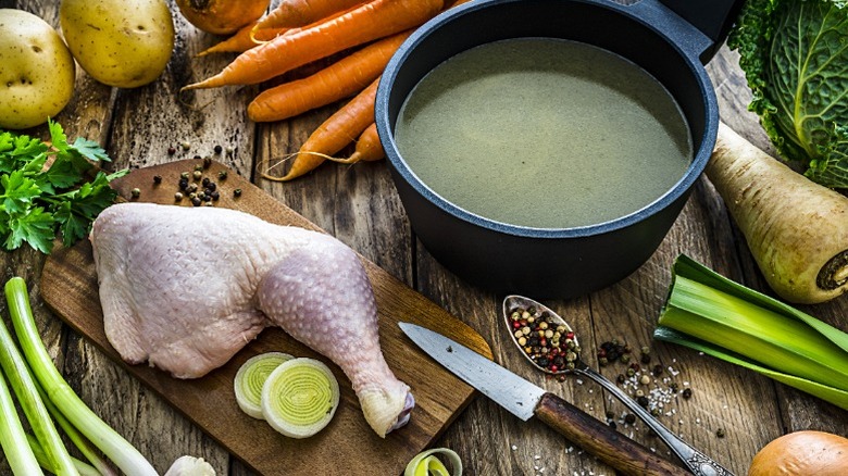 Chicken meat on a cutting board, surrounded by vegetables and a pan of water to make chicken stock.