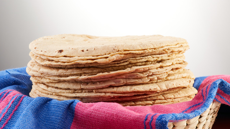 Pile of freshly made tortillas over a Mexican pink and blue cloth or napkin in a basket.