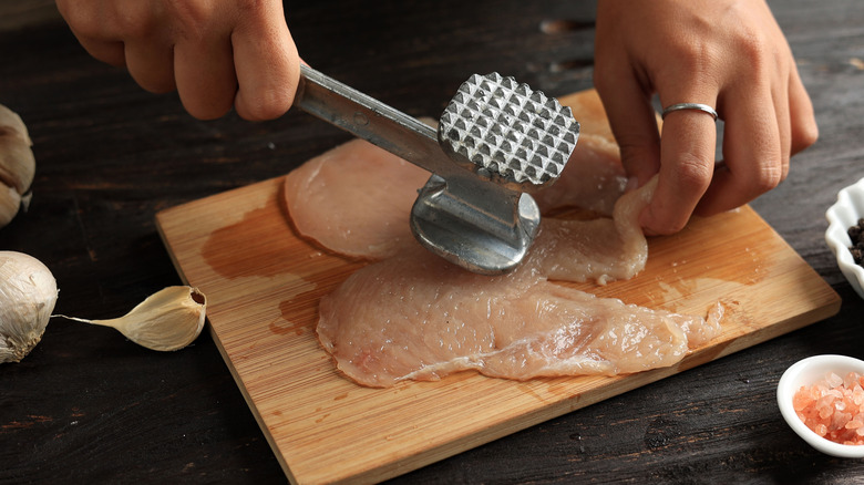 tenderizing chicken on small wooden board with garlic and salt