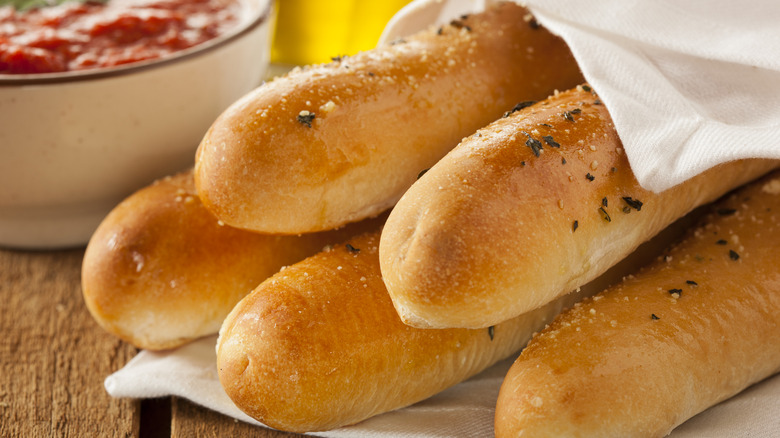 Breadsticks wrapped in a cloth with a bowl of marinara in the background