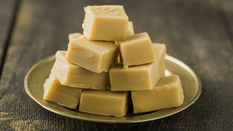 Squares of white chocolate fudge stacked on a gold plate on a wooden table.