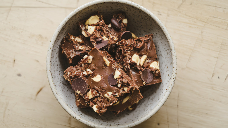 Portions of homemade fudge topped with nuts and chocolate chips in a grey bowl on a wooden table.