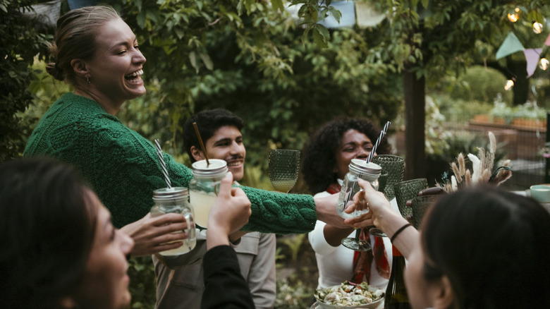 group of friends toasting mason jar glasses filled with drinks during outside picnic