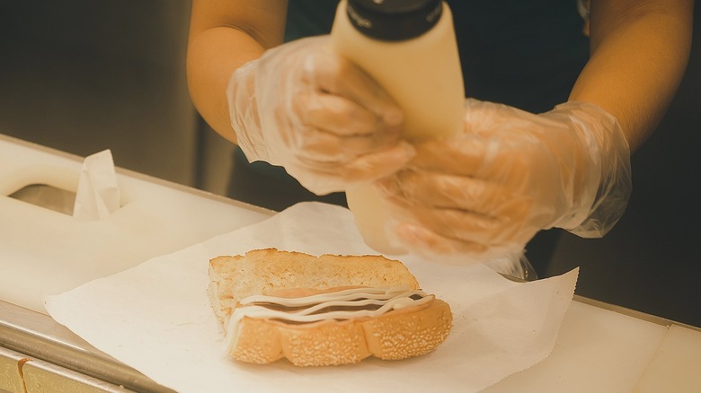 A worker at Subway applying sauce to a Subway sandwich