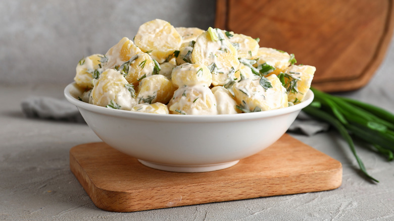 White bowl of potato salad on a wooden board