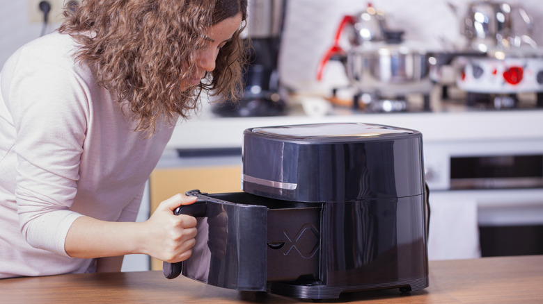 Woman leaning down to use air fryer.