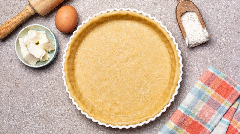 An unbaked pie shell surrounded by butter, flour, and eggs