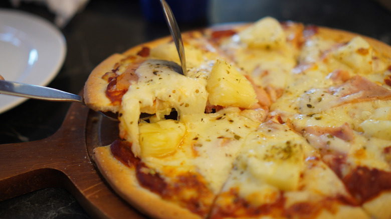 Someone picking up a slide of pineapple pizza on a serving dish