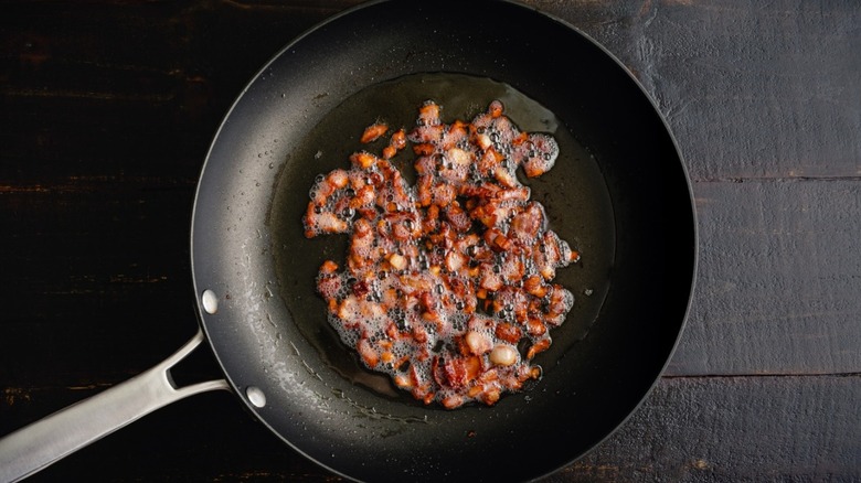 Bacon pieces sizzling in frying pan