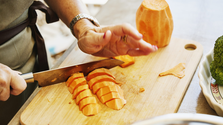 chef chops peeled sweet potato on board