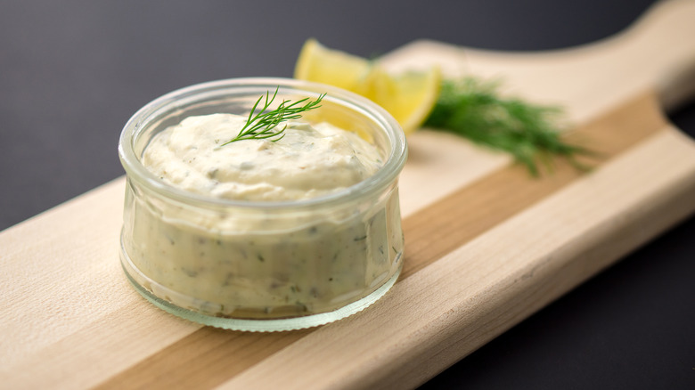 A little glass bowl of tartar sauce garnished with a sprig of dill