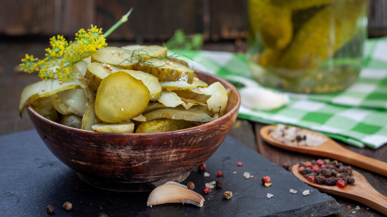 Wooden bowl of sliced pickles with jar in background