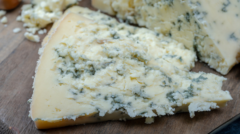 Slice of crumbly blue cheese on a wooden cutting board