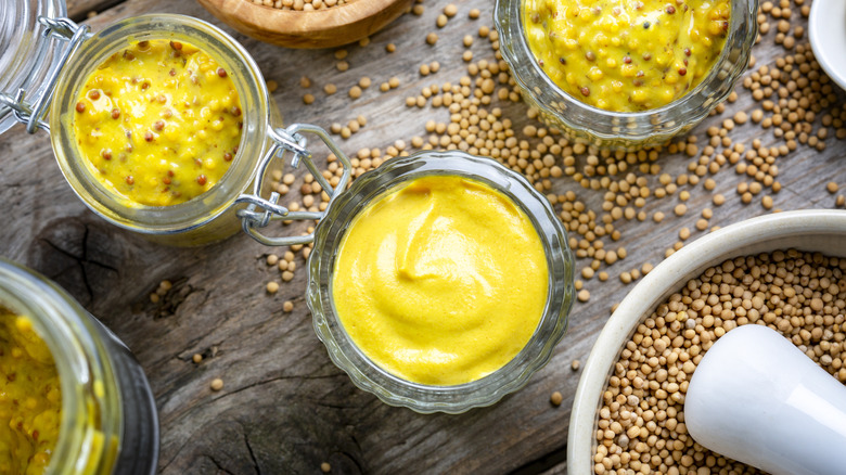 Different types of mustard in jars on a wooden surface.