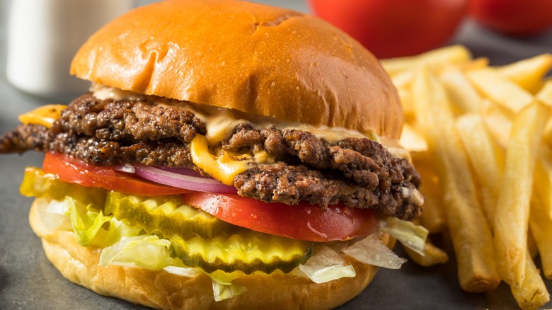 Smash burger with two patties, lettuce, pickle, and tomato on a bun with a side of fries