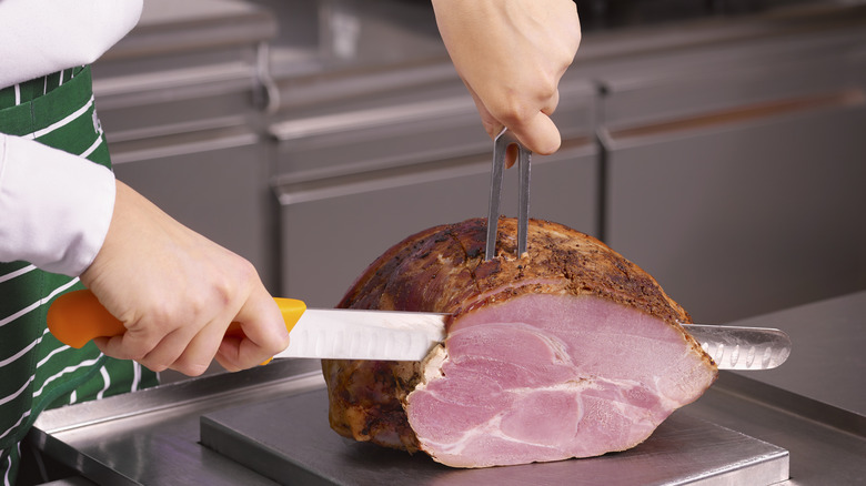 someone slicing ham on a metal board