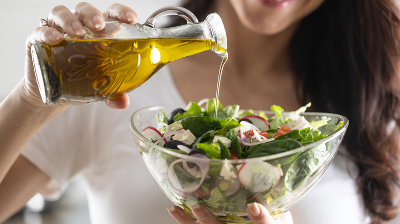 A person pouring olive oil onto a salad