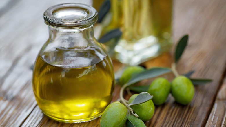 Olive oil in a small jar next to olives on a wooden surface