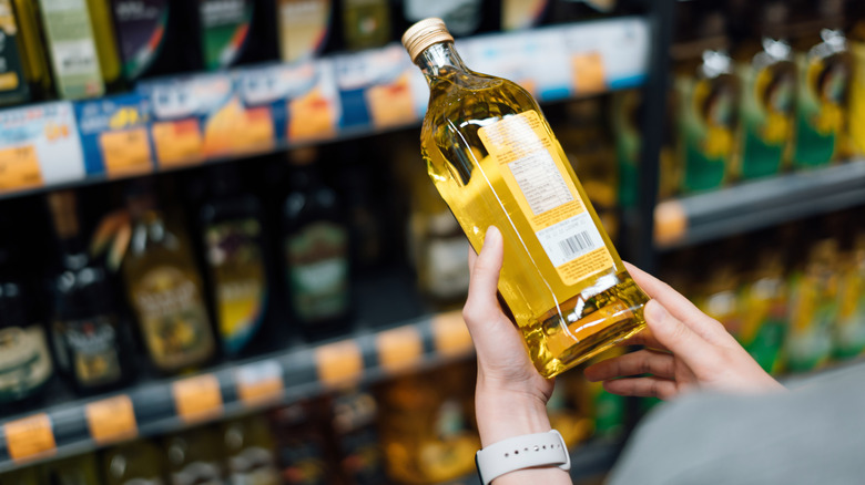 A person holding a small glass bottle of extra virgin olive oil in a grocery store aisle