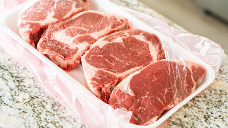 Raw steaks in their original packaging with the wrap torn partly off