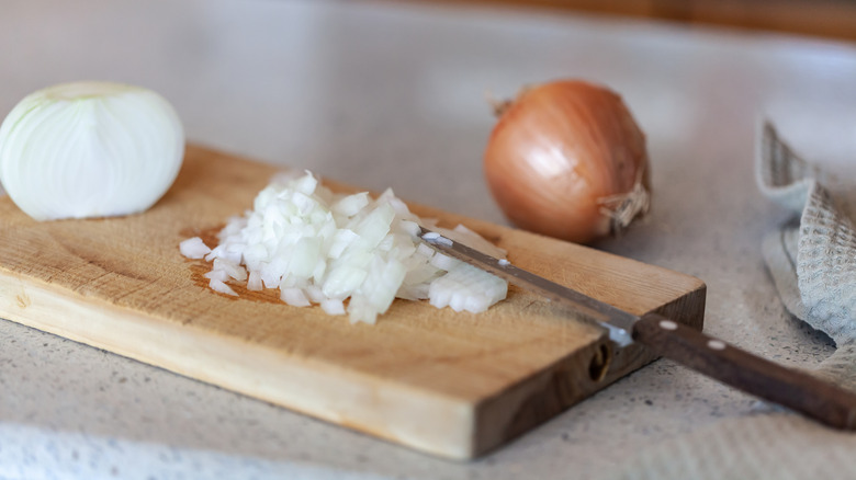 Half a chopped onion with a knife on a wooden board