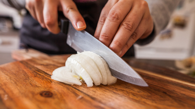 A person chopping a white onion on a wooden board