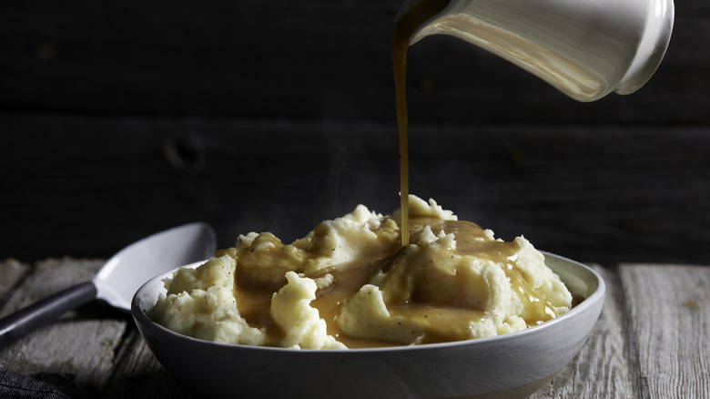 A jug pouring gravy on a bowl of mashed potatoes