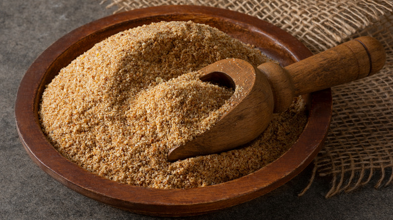 A brown bowl full of breadcrumbs with a wooden spoon in it