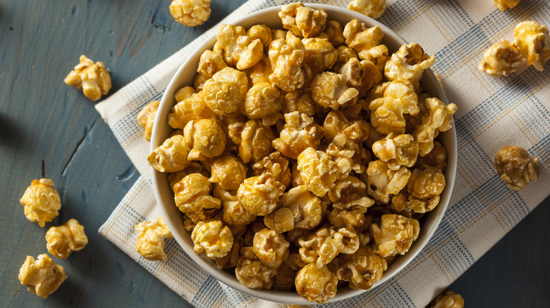 bowl of sugared popcorn on wooden table surrounded by scattered popcorn pieces